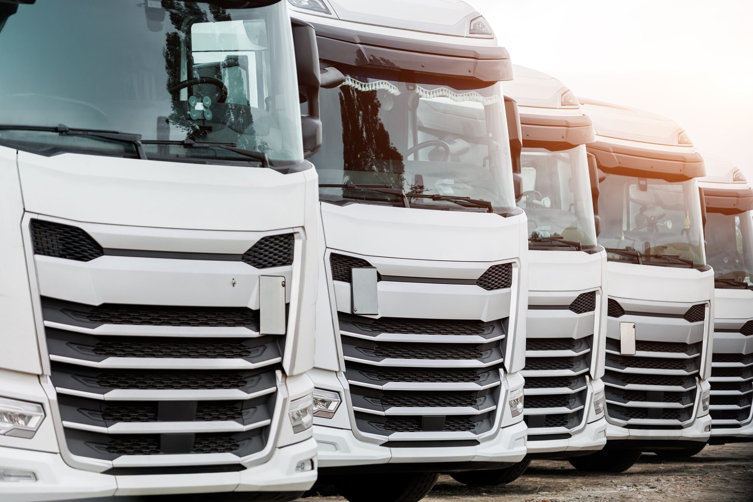 Frota de caminhões brancos alinhados em pátio de transporte, representando investimento e planejamento por meio de consórcio de caminhão para renovação de frota empresarial.