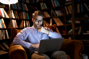 A foto de um homem sentado em seu escritório com o notebook no seu colo pesquisando se consórcio vale a pena